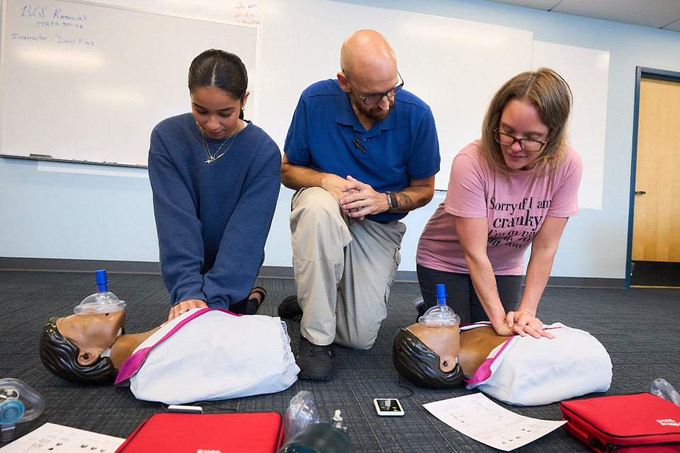 CPR training session with two students and an instructor performing chest compressions on CPR mannequins.